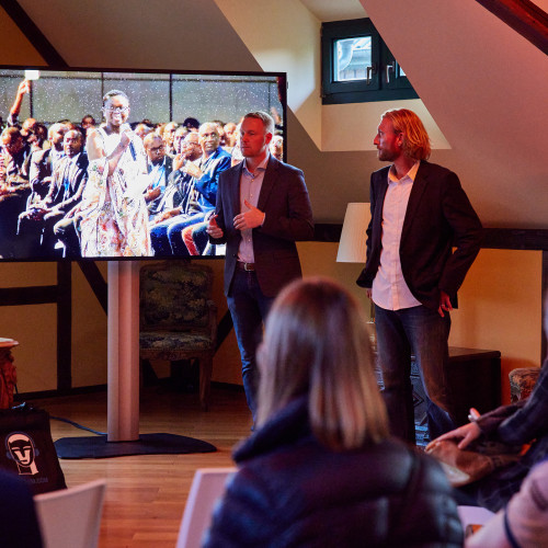 Zwei Männer stehen vor einem Fernseher und halten einen Vortrag